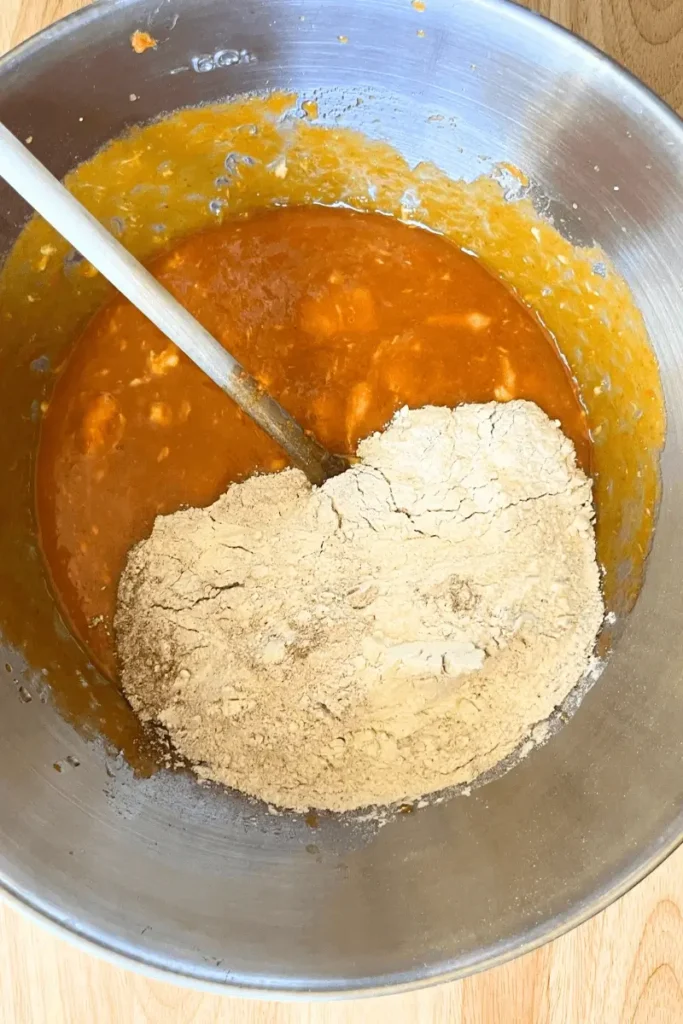 Adding flour, baking powder, cinnamon, and salt to wet mixture — making soft and spiced sourdough pumpkin bar batter.