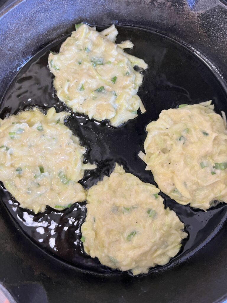 Sourdough zucchini fritters frying in a cast iron skillet.