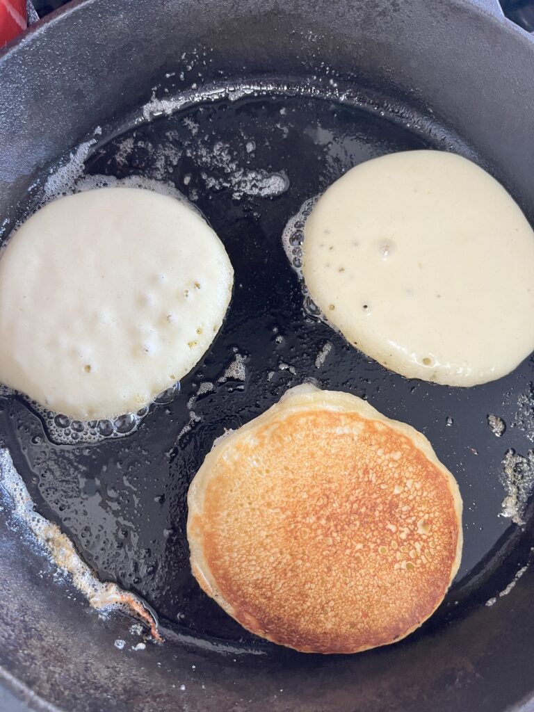 Buttermilk pancakes frying on a cast iron skillet. 