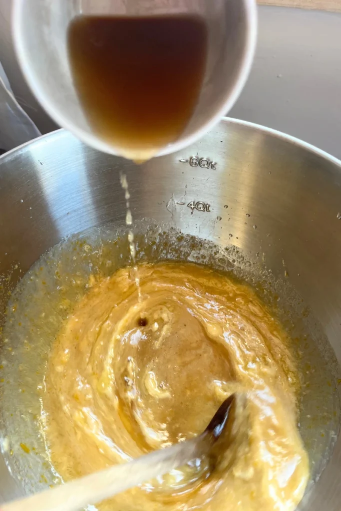 Pouring apple cider into the batter for Sourdough Apple Cider Muffins.