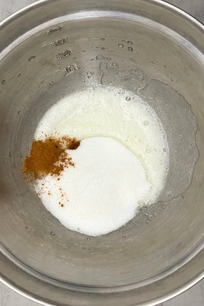 Whisking a large egg white in a glass bowl until frothy for candied pecans.