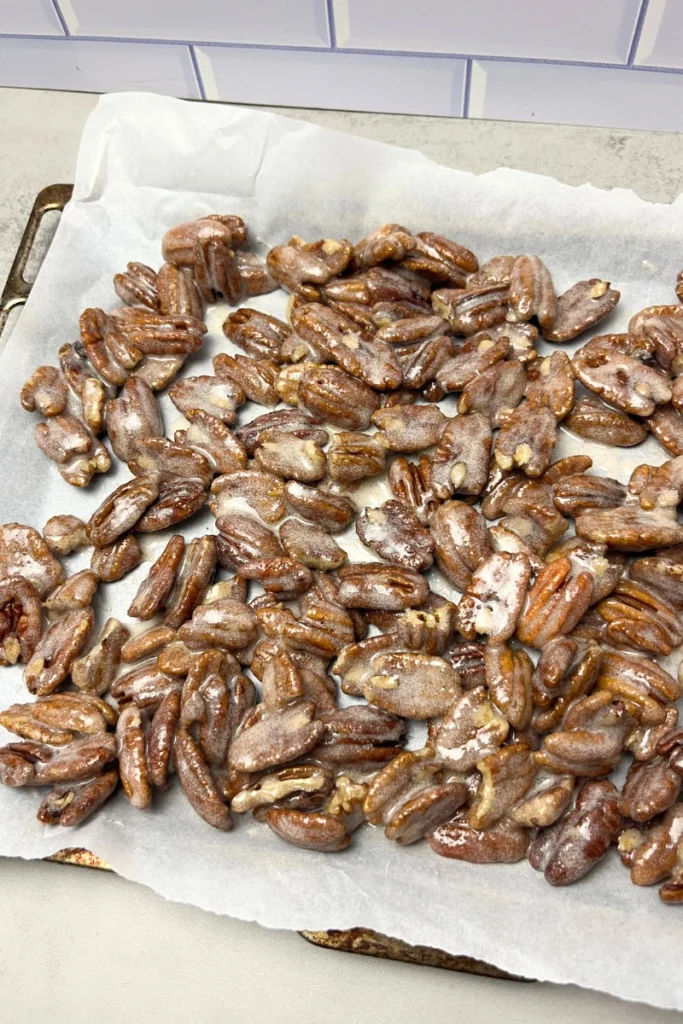 Candied pecans spread in a single layer on a parchment-lined baking sheet ready to bake.