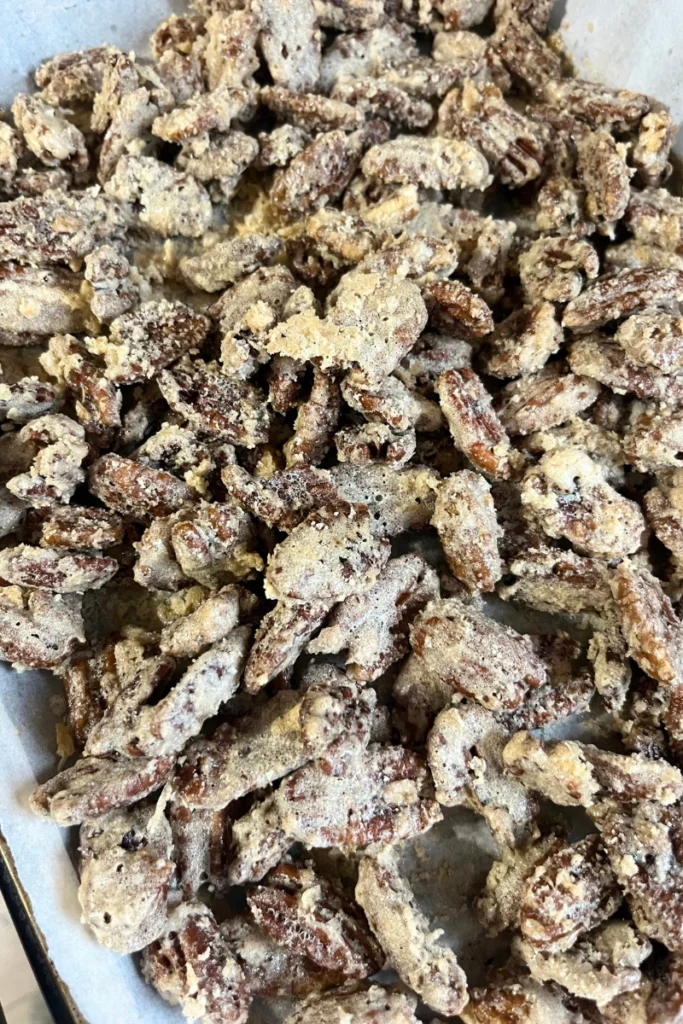 Golden candied pecans cooling on a baking sheet after baking.