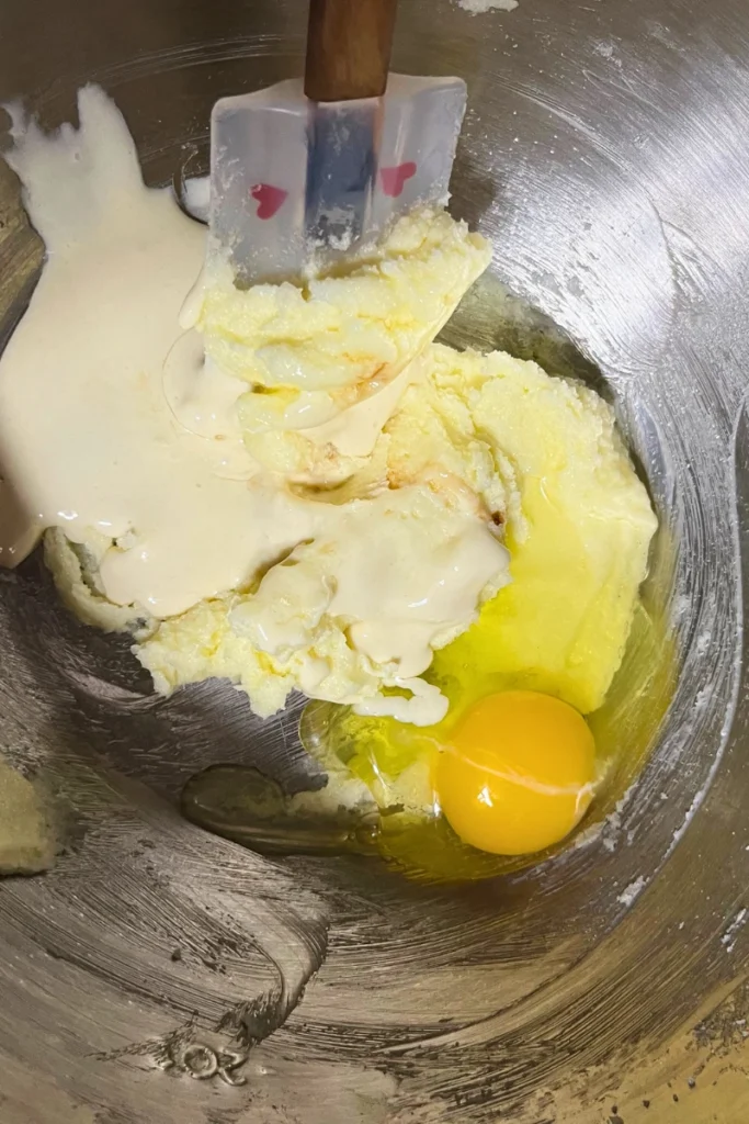 Egg, vanilla extract, and active sourdough starter added to creamed butter and sugar in a bowl, being mixed until smooth for sourdough sugar cookies.