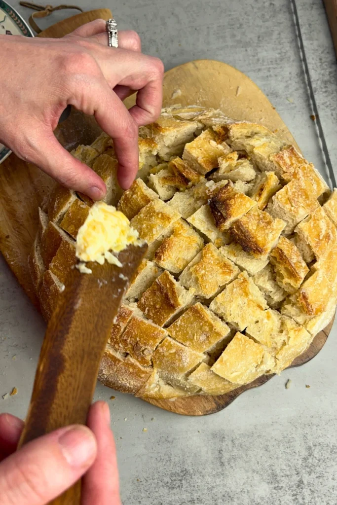 Filling a baked sourdough boule with garlic butter in the criss-cross cuts.