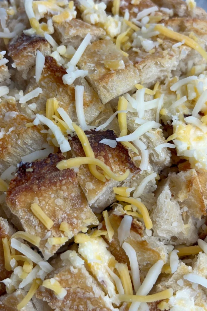 Sprinkling shredded cheese into the criss-cross cuts of a baked sourdough boule.