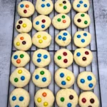 Soft sourdough sugar cookie on a cooling rack, about 1 tablespoon in size, topped with colorful M&M candies, lightly golden edges, tender center.