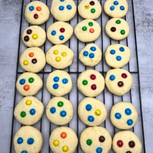 Soft sourdough sugar cookie on a cooling rack, about 1 tablespoon in size, topped with colorful M&M candies, lightly golden edges, tender center.