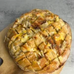 Garlic cheese sourdough pull-apart bread baked on a wooden cutting board.