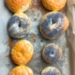 Freshly baked sourdough bagels on a parchment-lined baking sheet, golden brown and chewy,.