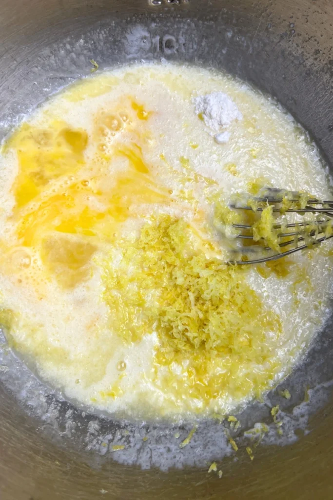 2 Bowl of wet ingredients for sourdough lemon poppy seed muffins mixed together, including sourdough discard, eggs, milk, melted butter, sugar, lemon juice, lemon zest, and vanilla extract, whisked until smooth.