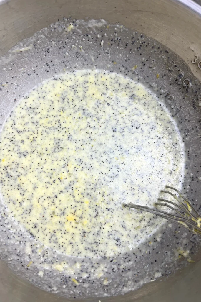 3 Bowl of muffin batter with dry ingredients added, showing flour, baking powder, baking soda, salt, and poppy seeds being mixed into wet sourdough lemon muffin batter.