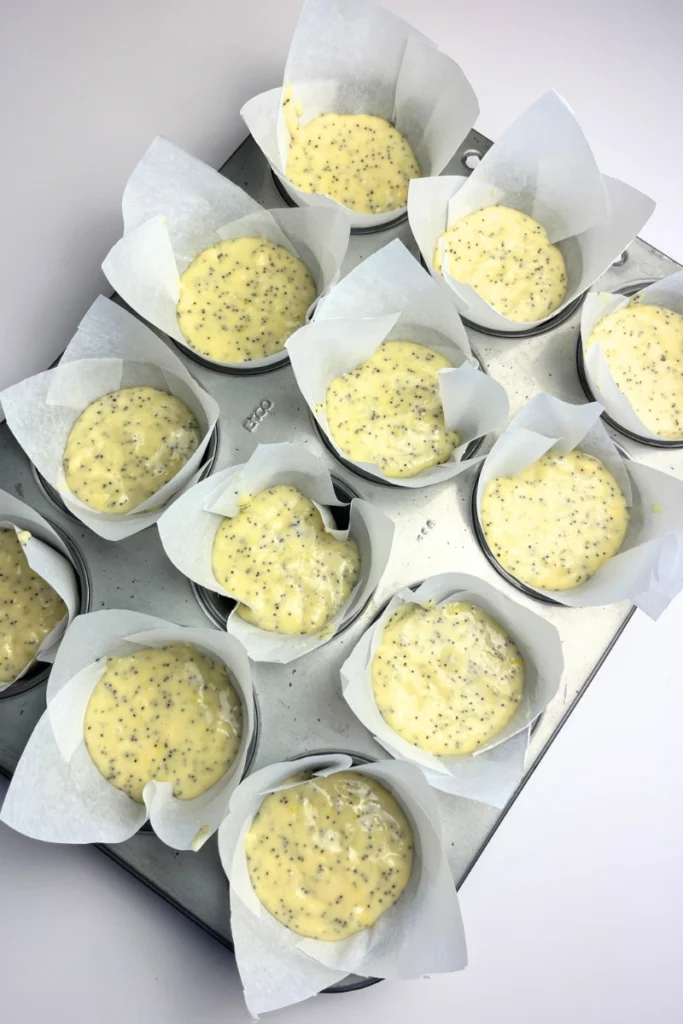 4 Muffin tin filled with sourdough lemon poppy seed muffin batter in paper liners, ready to bake with evenly portioned batter in each cup.