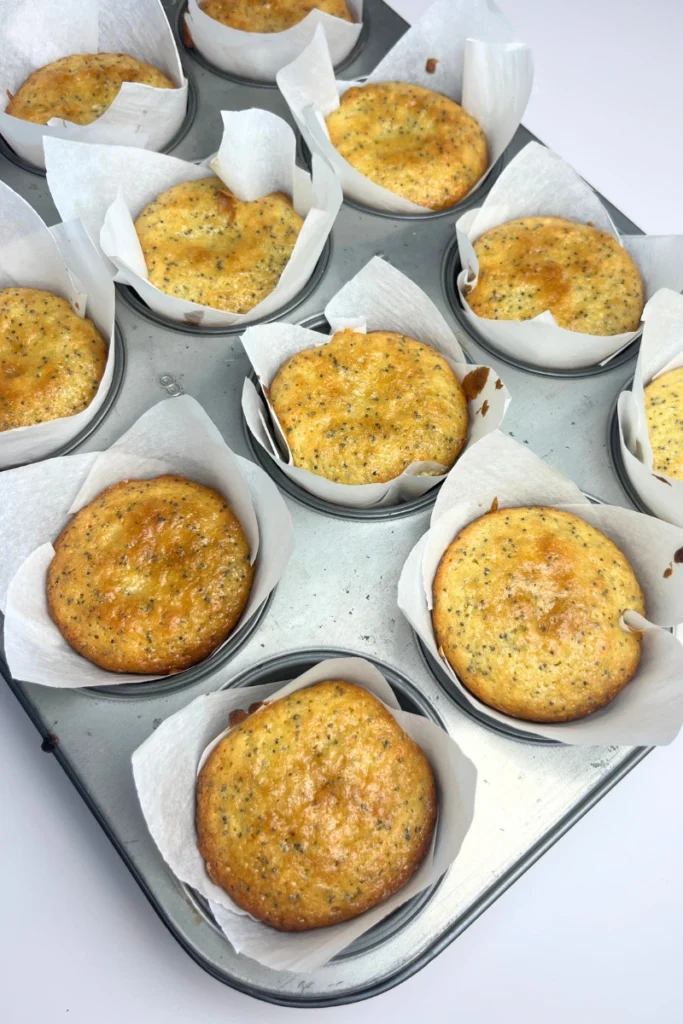 7 Freshly baked sourdough lemon poppy seed muffins in a muffin tin, golden brown tops with a light rise and bakery-style texture.